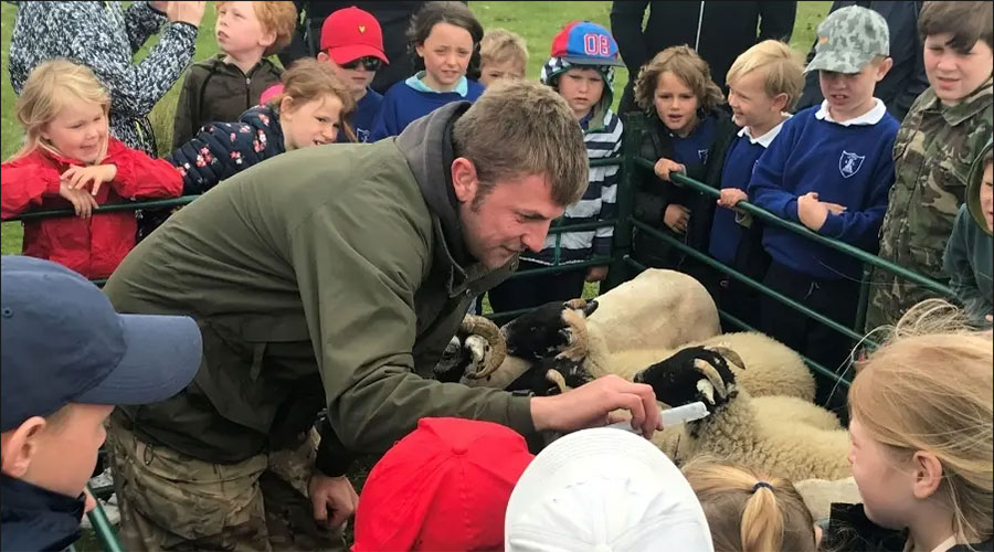 A speaker talking to children next to sheep