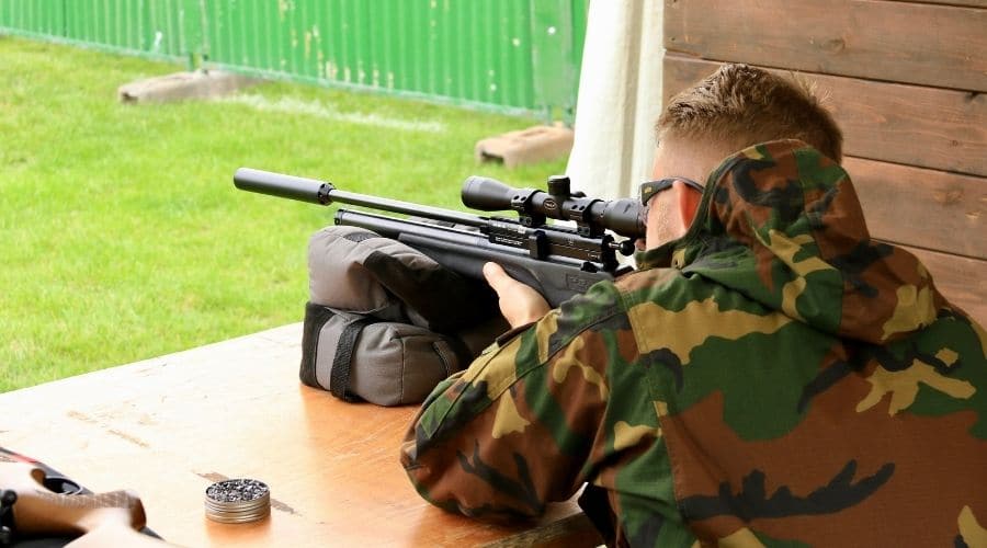 An air rifle shooter aiming down the scope of a rifle