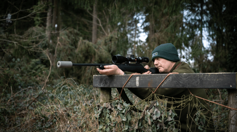 A deer stalker aiming down the rifle scope