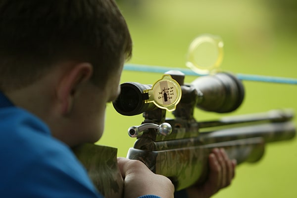 A child aiming down the scope of an air rifle
