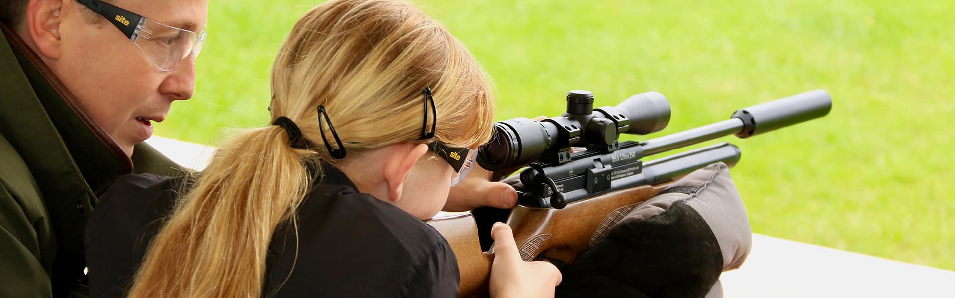 A girl aiming down the scope of an airgun with a coach beside her