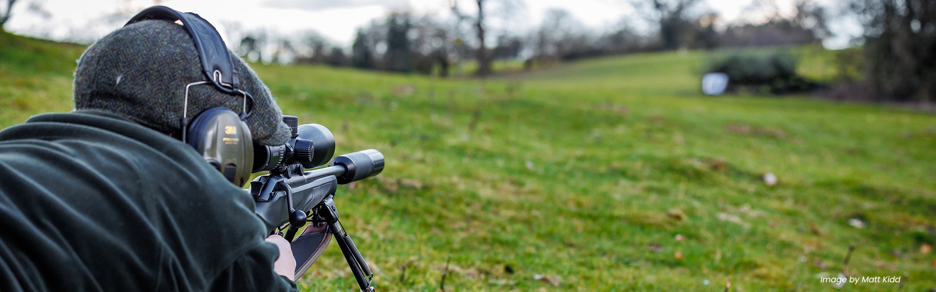 A deer stalking lying down aiming through the scope of their rifle