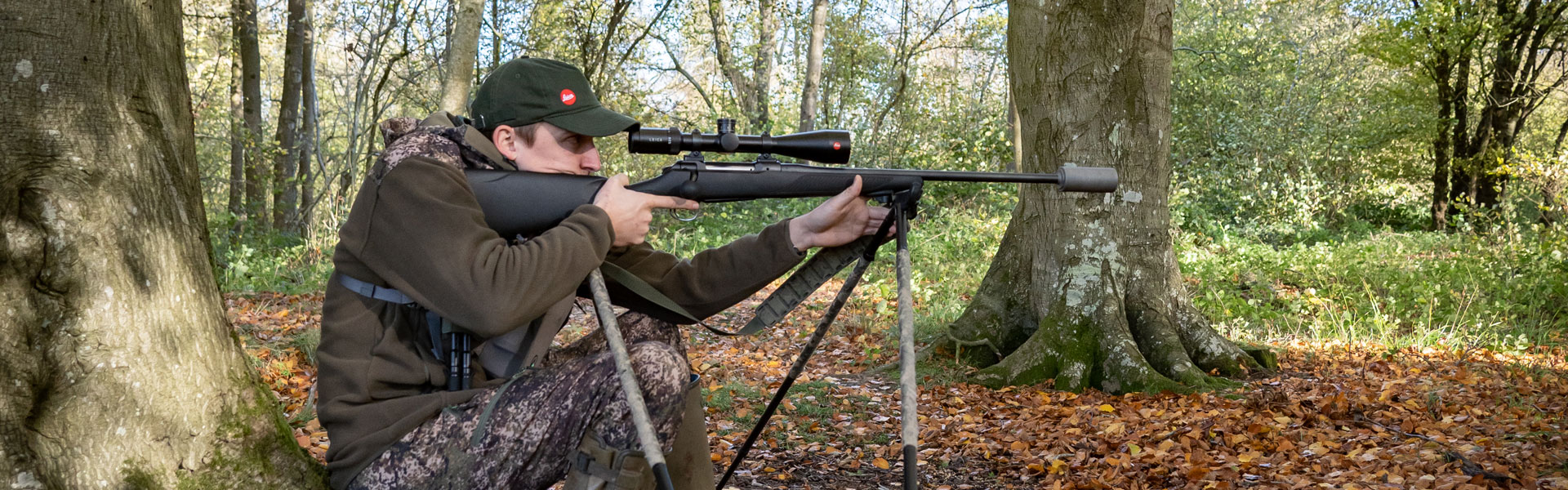 A deer stalker aiming down their rifle scope