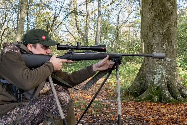 A deer stalker aiming down their rifle scope