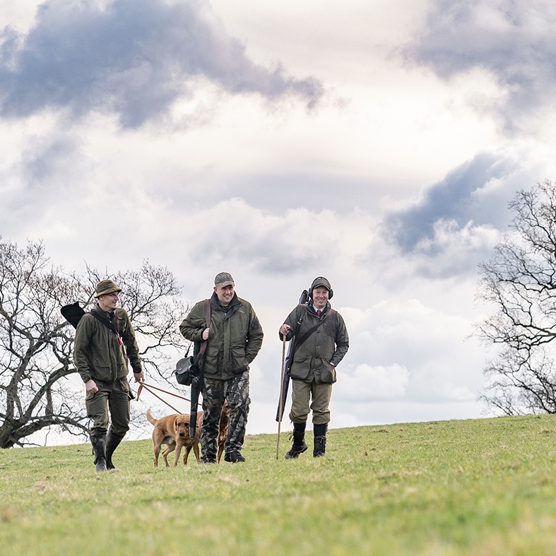 Three game shooters walking across a field with their gundog