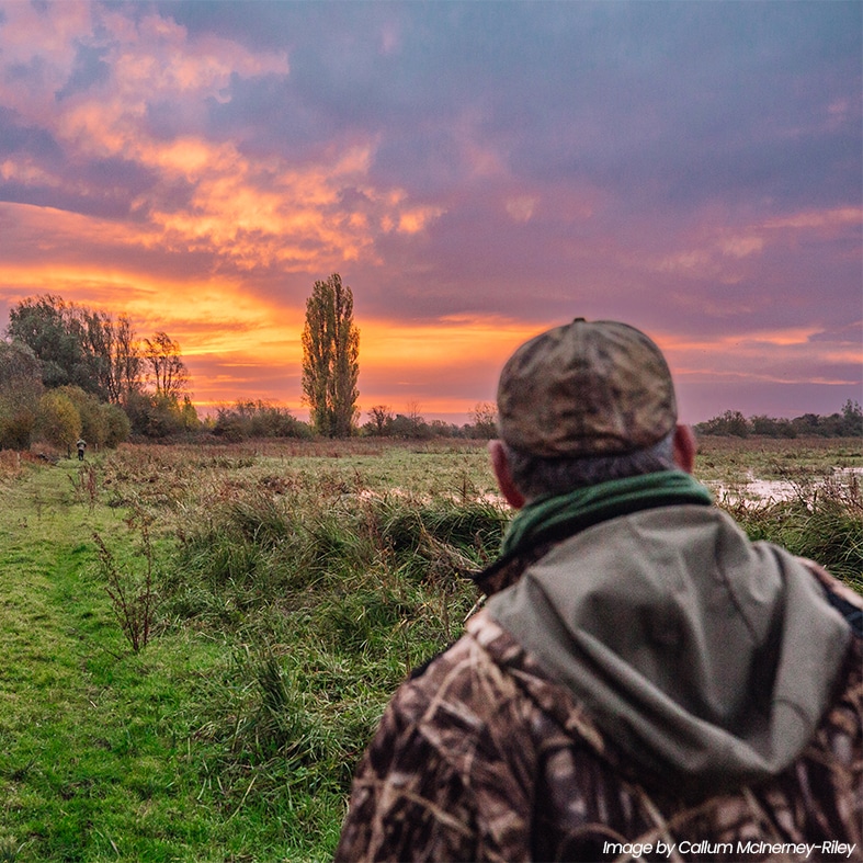 A wildfowler looking across a field at dawn