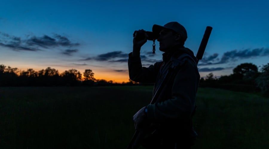 A deer stalker looking through binoculars at dusk