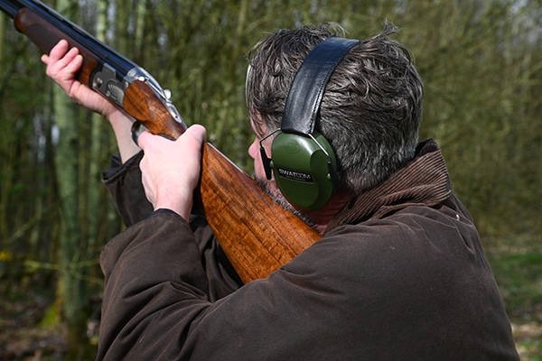 A shooter aiming a shotgun wearing hearing protection