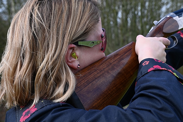 A shooter aiming a shotgun wearing hearing protection