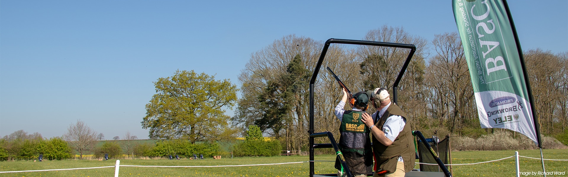 A BAC coach with a student firing a shotgun