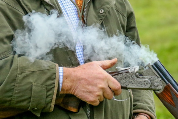 A shooter holding a shotgun while smoke comes out of the barrels