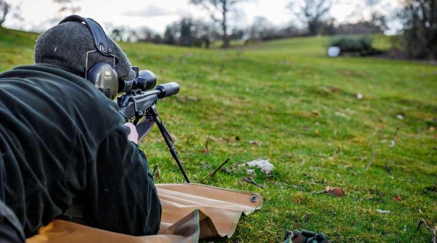 Rifle shooter lying down aiming down a scope