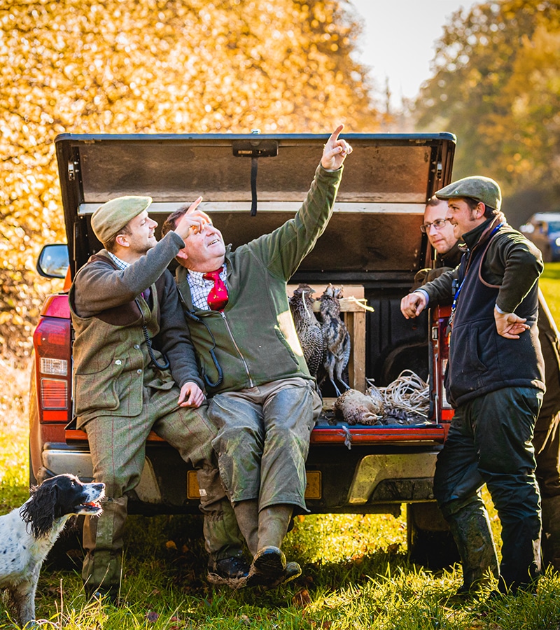 A group of shooters sitting in the back of an open truck talking and pointing to the sky