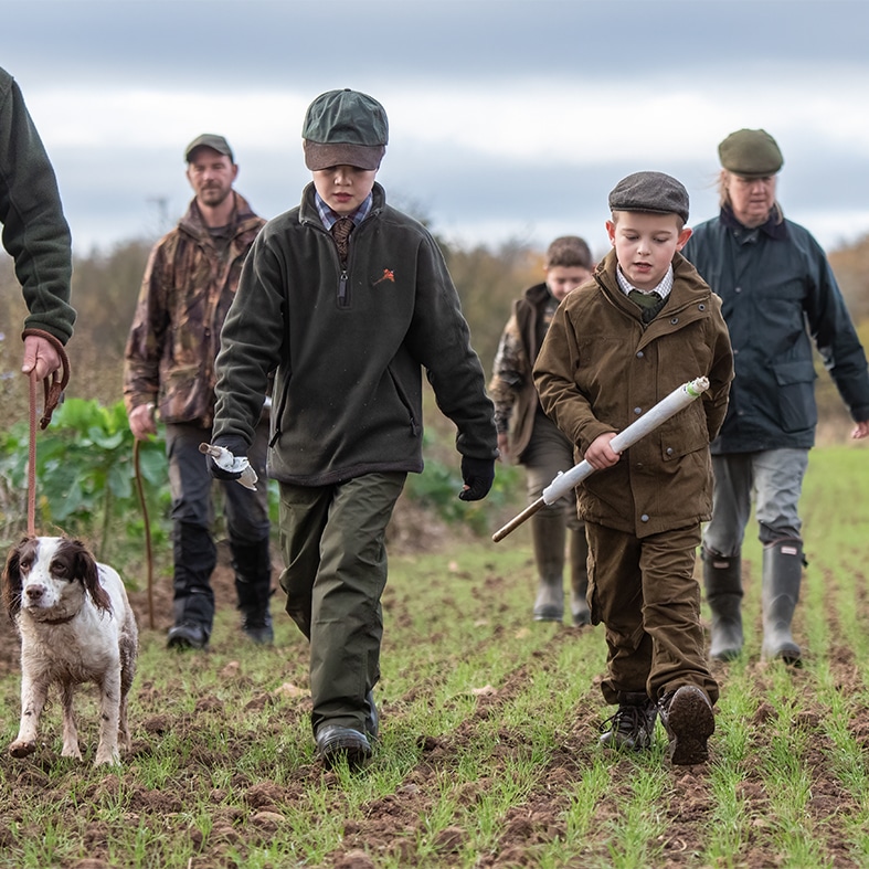 A group of game shooters and two children walking through a field holding beater flags