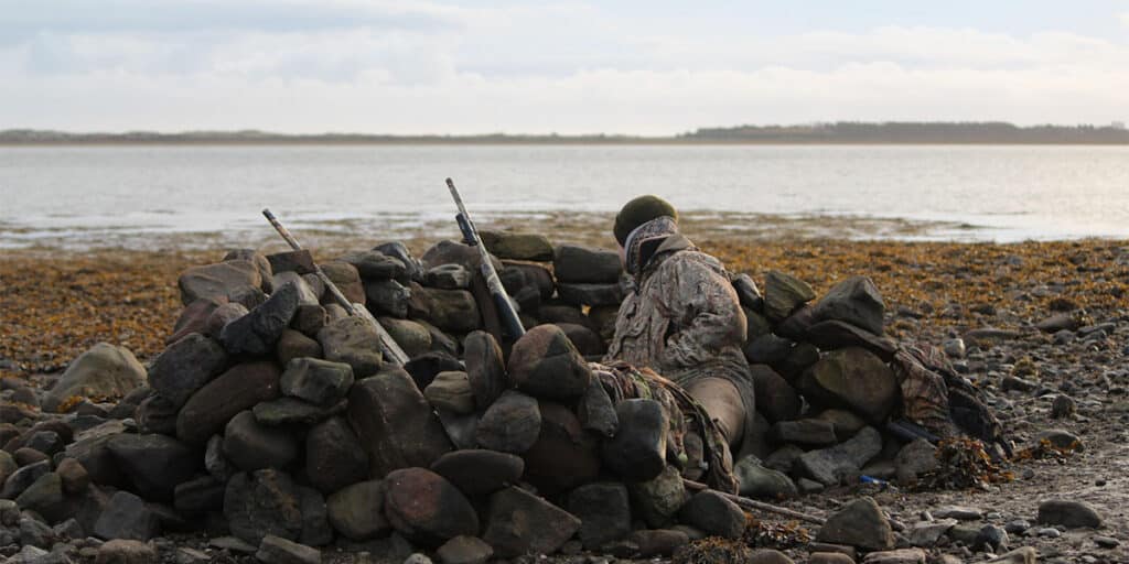 A wildfowler crouched behind a stone hide