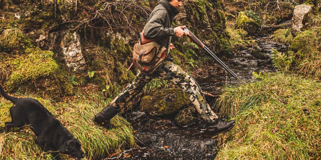 A game shooter crossing a small stream with their gundog