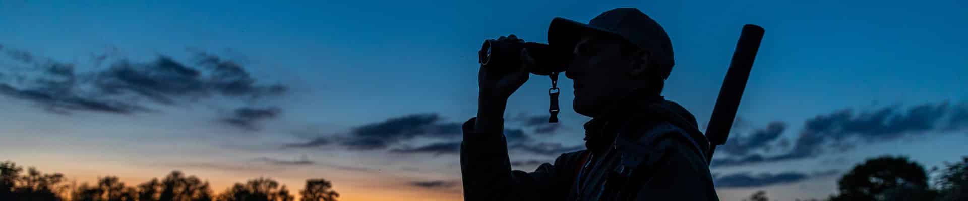 Night deer stalker looking through binoculars