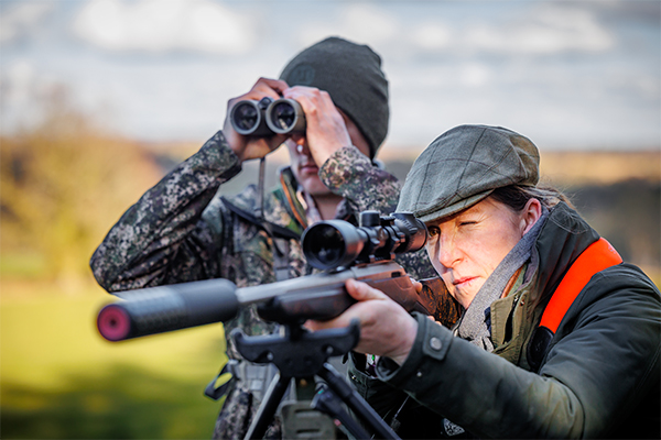 Shooter aiming down a scope of a sound moderated rifle