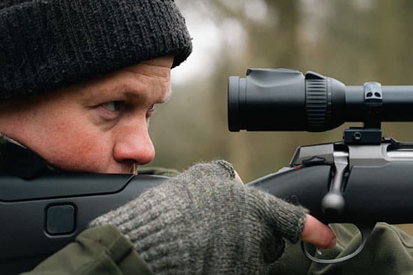 Deer stalking aiming down the scope of a rifle