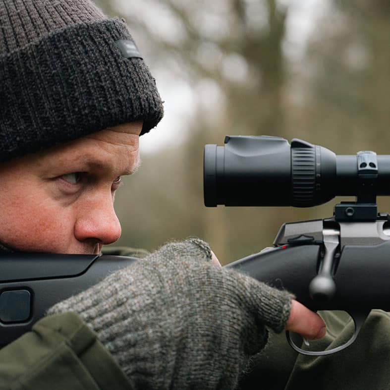 Deer stalking aiming down the scope of a rifle